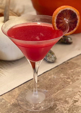 Close-up shot of a pink drink in a martini glass, with a garnish of a blood orange slice.