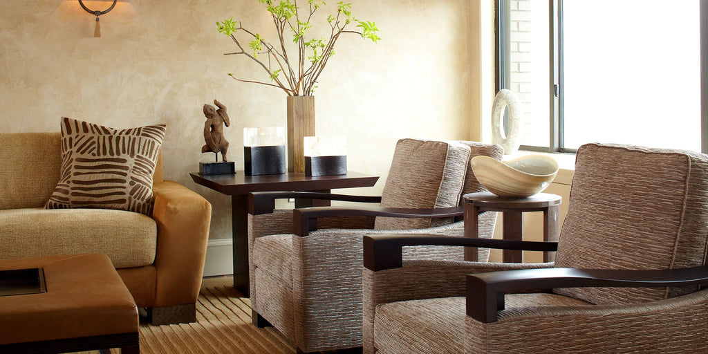 An elegantly decorated room in soft golds , neutrals and whites. A sofa is on the left, with a side table next to topped with decorative accessories. Two arm chairs, with an accent table between them, complete the room.