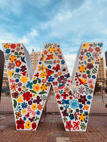 Outdoor picture of a large sculptural W decorated in a colorful floral pattern. Photo by Lona on Unsplash.