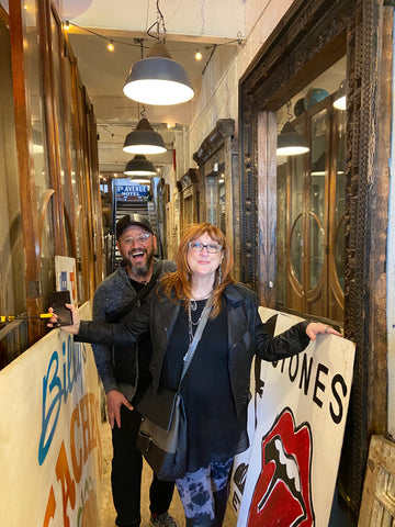 Robin Baron and Yudi Kaufman pose in a hallway with decorative art around them.