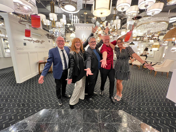Robin Baron poses with the Metropolitan Lighting Showroom team in a room filled with lighting fixtures.