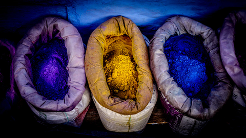 3 sacks with brightly colored powder that is used to dye fabric. Purple, yellow, and blue. 