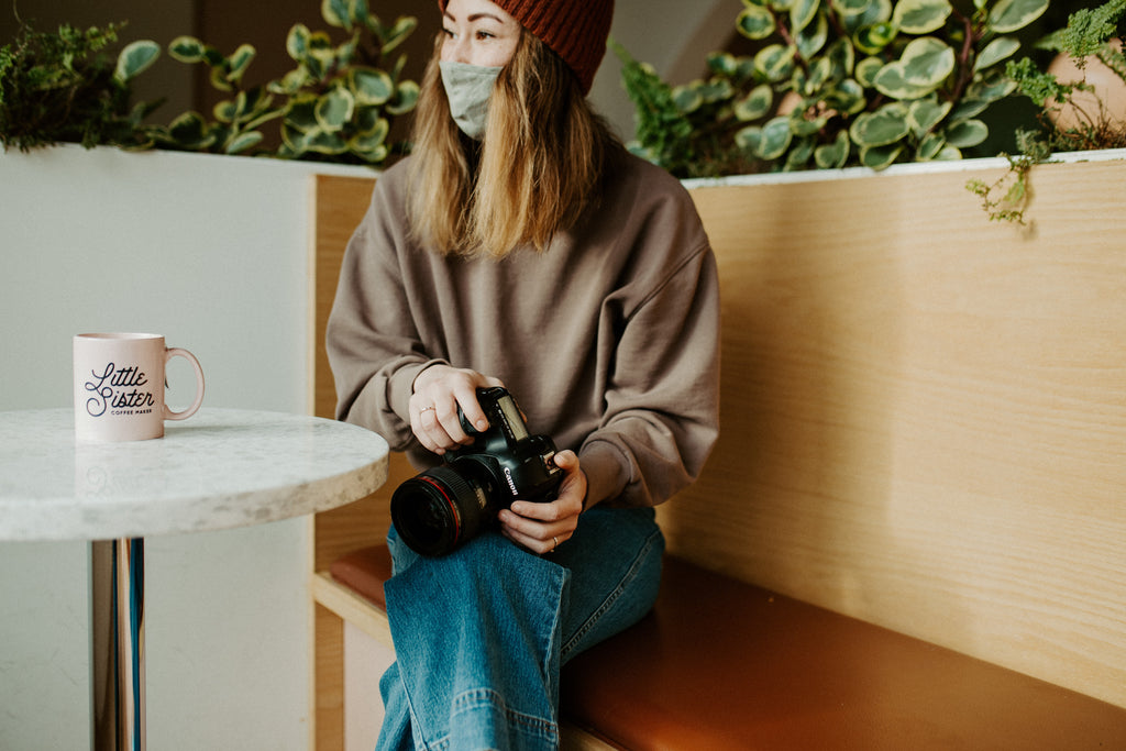 Girl sits on bench with camera in lap, wearing mask and looking away from the camera