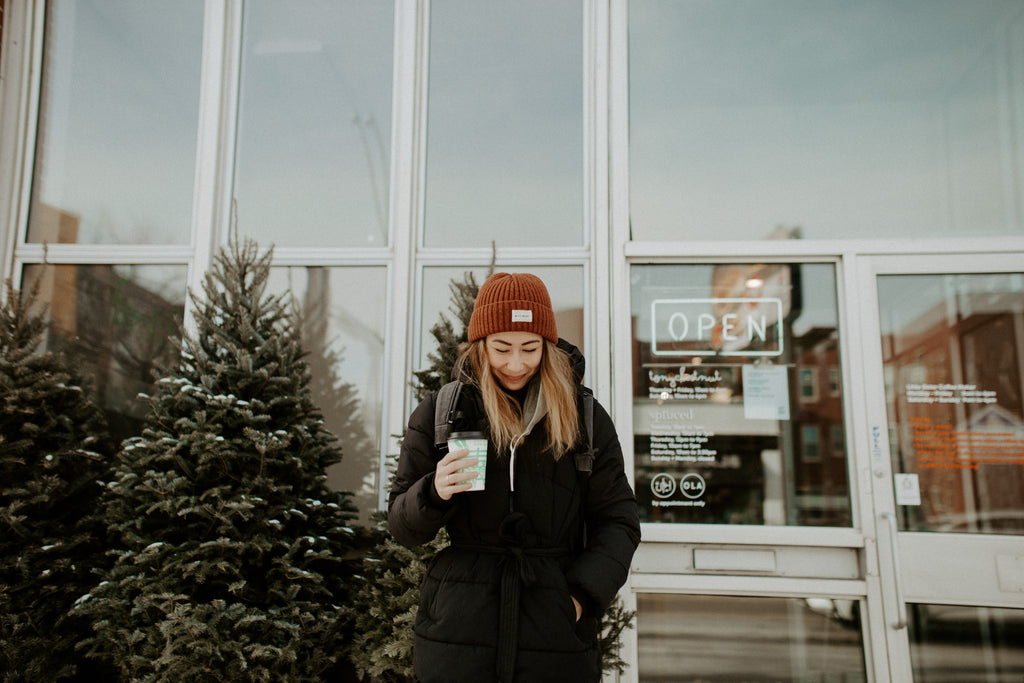 Girl holds coffee cup, smiling, while standing in front of coffeeshop.