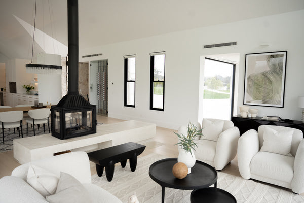 A spacious living room area with white, beige and black used in the design. There is a central fireplace in the middle of the living room.