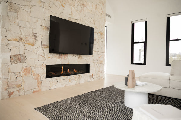 a living room with beige wall cladding. There is a television hanging on the wall with stone cladding.