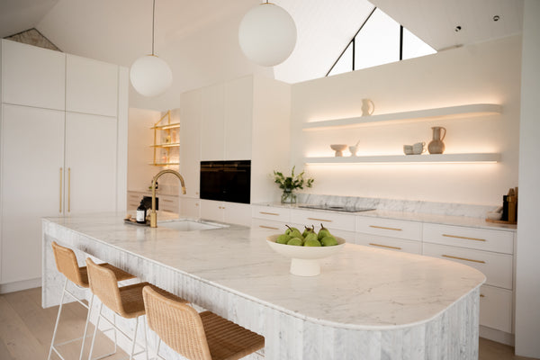 a kitchen with white marble used on the counter and splashback. The features use gold and black as complimentary colours.