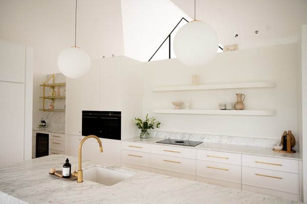 a modern kitchen design with white marble used on the countertop and splashback. The kitchen tap and drawer handles are gold colour.
