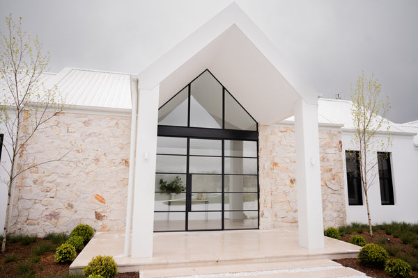 a medium shot of a modern style home design facade with white walls, black window frames and beige stone cladding.