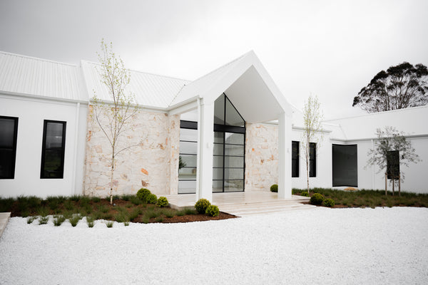 a modern style home design facade with white walls, black window frames and beige stone cladding.