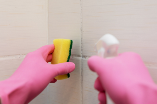 Someone wearing pink gloves cleaning tiles with sponge