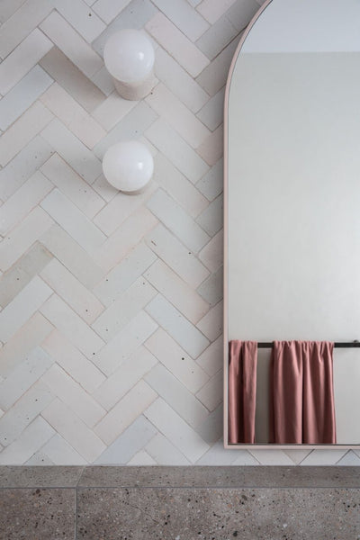 bathroom wall tiling with grey ceramics laid in herringbone style. Half of the mirror is visible.