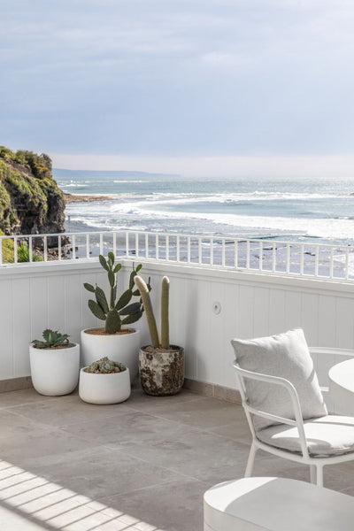 balcony overlooking the ocean with marble flooring and a few plants and a white chair