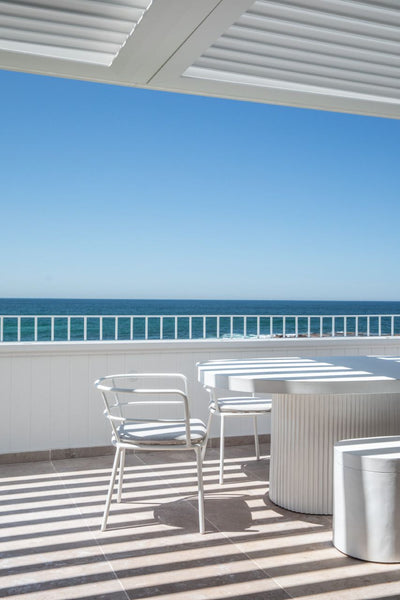 Balcony overlooking the ocean with a table and few chairs on marble flooring