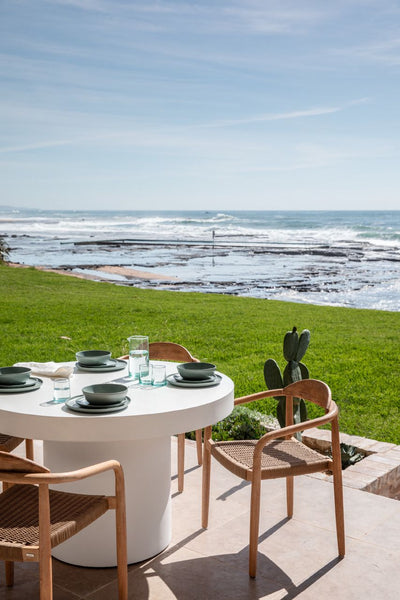a round table with two chairs near the beach on the backyard of a beach house