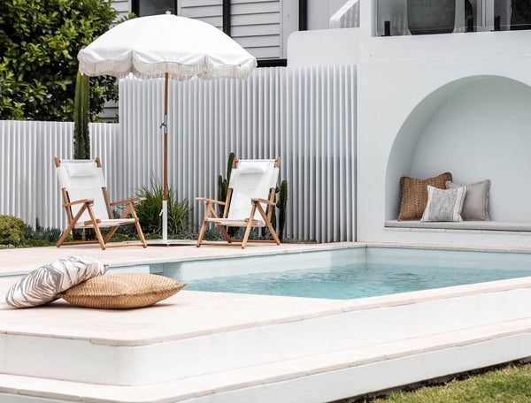 outdoor swimming pool with light beige marble pavers. There are some chairs in the far end.