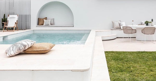 outdoor swimming pool with light beige marble pavers. There are some chairs in the far end.
