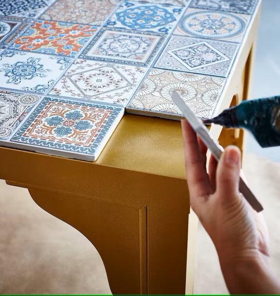 Hands of someone putting on glues on tiles. The table is visible at the back.