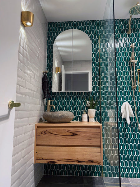 bathroom sink area with curved mirror. One wall has white ceramic tiles and the wall behind the mirror is green mosaic tiles.