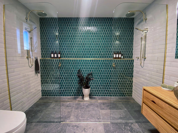bathroom design with green fan-shaped porcelain mosaics on a feature wall and white subway tiles on the other walls. The flooring is grey porcelain tiles.