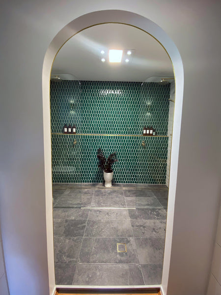 an arched entrance into a bathroom with green mosaic tiles on the wall across the entrance.