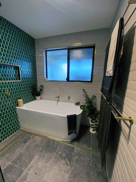 bathroom with a white bathtub. There is a window on top of the bathtub and the wall behind the bathtub is tiled with green mosaics.