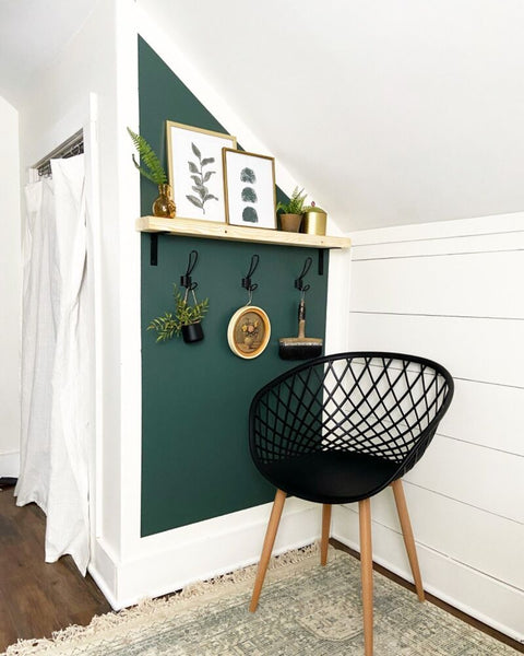 a cosy-looking corner with a brown low chair and a green feature wall with decoration items hanging from it.