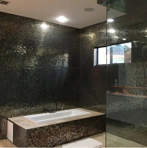 bathroom with dark and shiny glass mosaic tiles. There is a white bathtub in the bathroom.