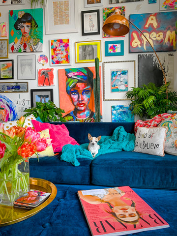 a vibrant and colourful room with many art pieces hanging on the wall. There is a blue sofa in the room with a dog sitting on it. 