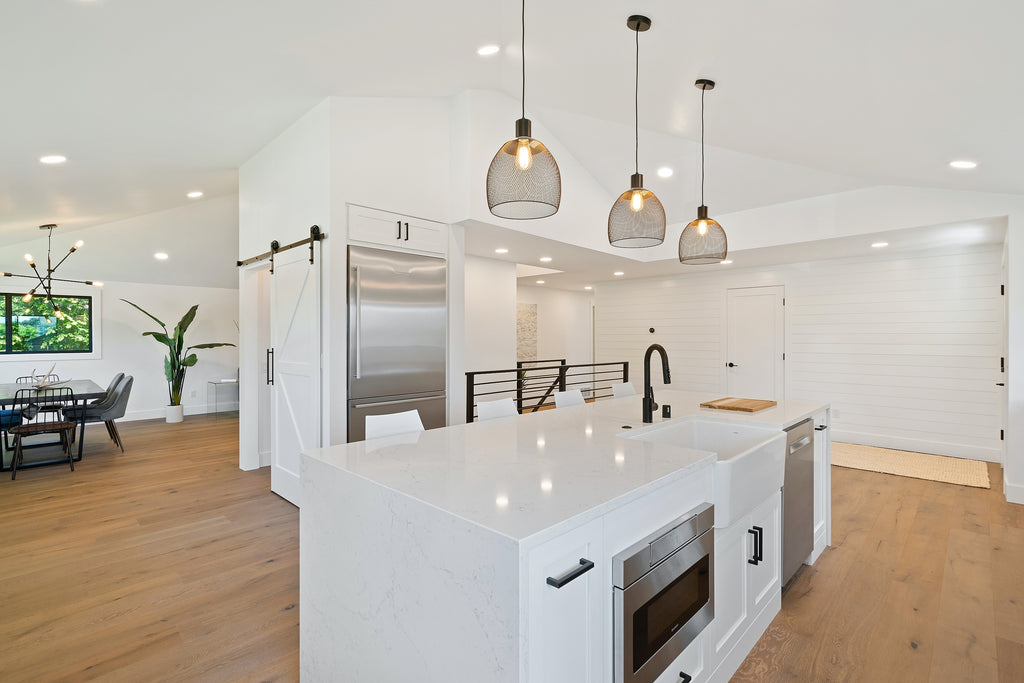 open space kitchen with white and sleek looking countertop and timber flooring