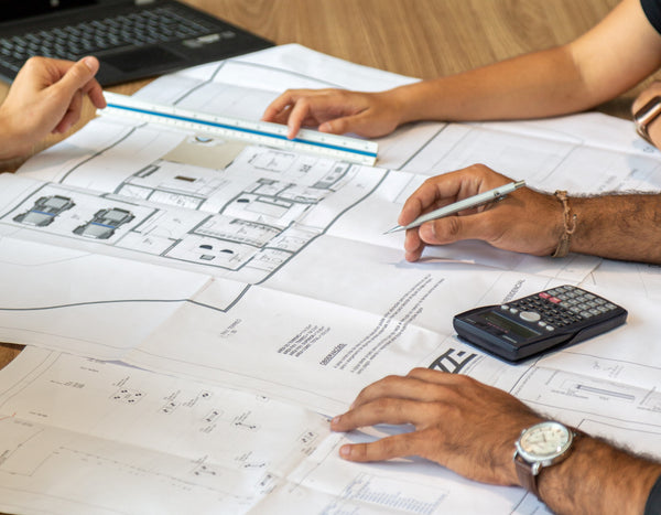 a few pair of hands on architectural planning maps laid out on a table