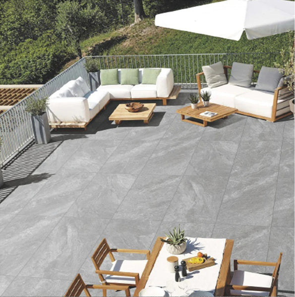 outdoor patio area with large grey porcelain tiles on the floor. There are a few couches visible.