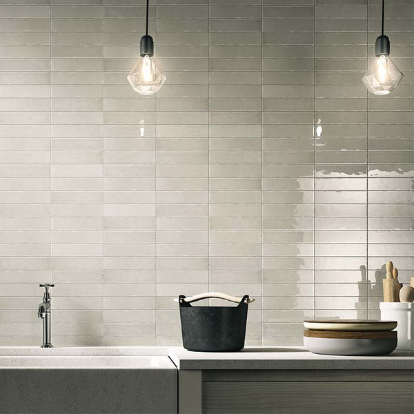 A kitchen splashback with grey ceramic tiles. There is a black bucket on the counter.