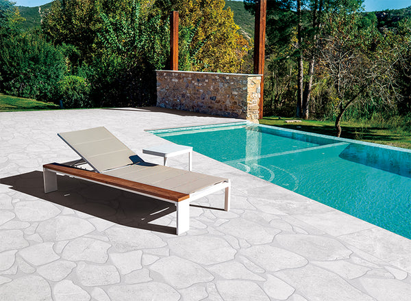 outdoor pool area with beige porcelain paver. There is a pool chaise lounge next to the pool.