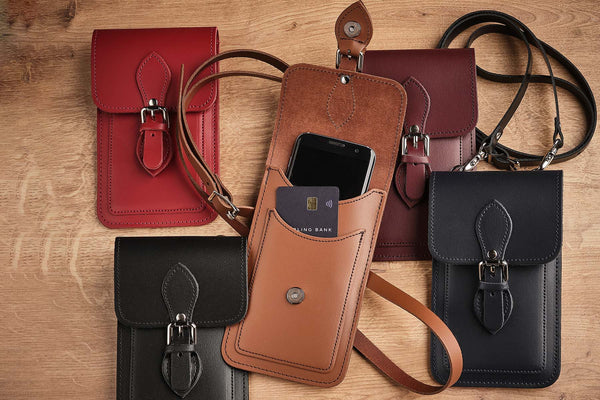 handmade leather mobile phone pouch in an assortment of different colours on a wooden table
