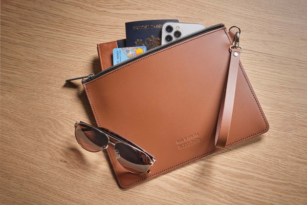 leather folio case with phone and travel documents placed inside and sunglasses on top