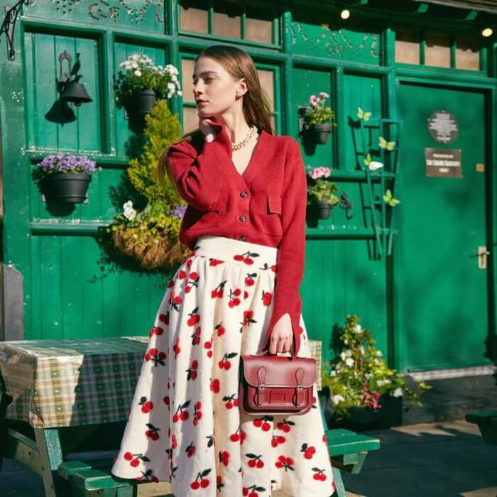 https://cdn.shopify.com/s/files/1/0315/0217/2298/files/Woman_wearing_white_skirt_with_cherries_holding_a_Oxblood_Midi_Satchel_Handbag.jpg?v=1666606220