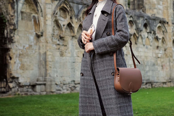 close up of person wearing long tailored coat and handmade leather saddle bag in brown