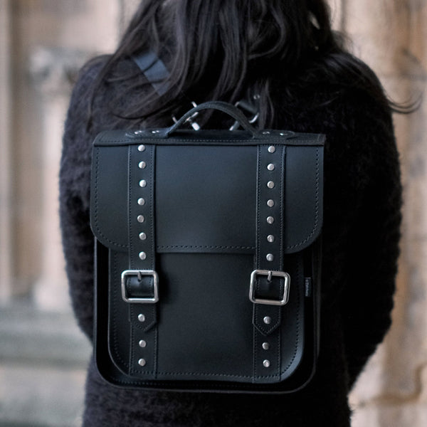 person wearing black studded backpack stood in front of a gothic building