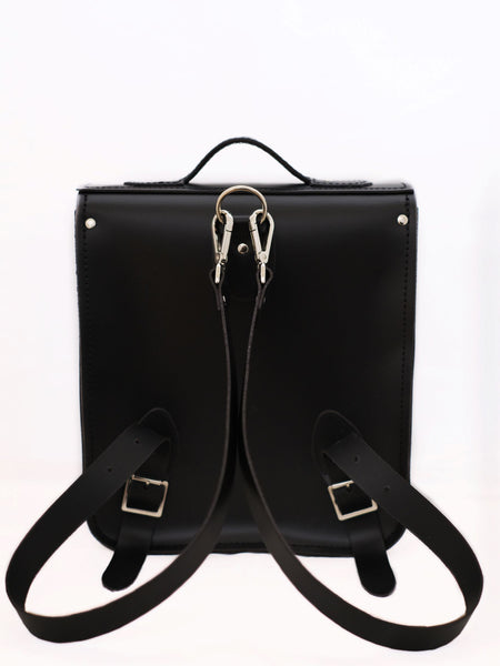 close up of back of black leather satchel backpack showing detachable straps on a white background