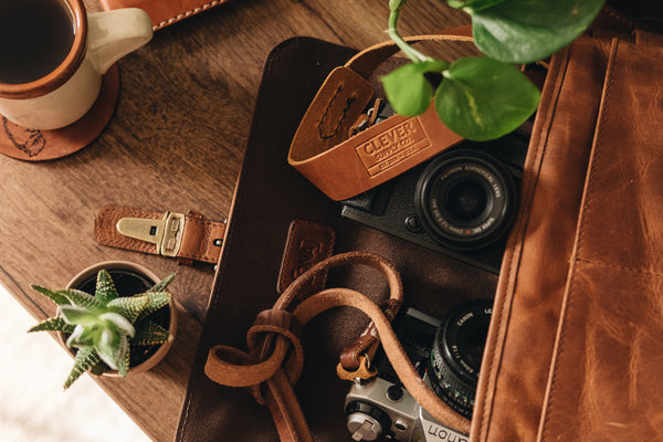 leather camera bag with two cameras and camera straps, a plant and cup of coffee