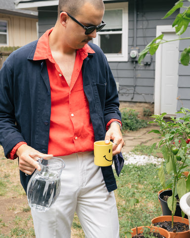 Man in linen shirt and jacket watering plants.