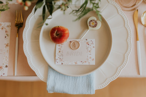 White heart shaped lollipop with a purple edible daisy on a white plate with a peach