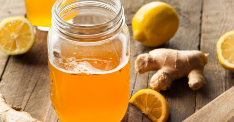 kombucha beverage in glass mason jar next to a lemon and ginger root