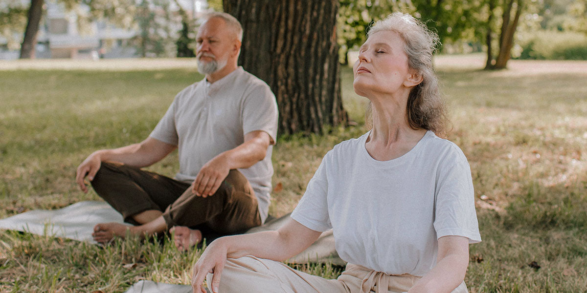 eine ältere Frau und ein älterer Mann, meditierend im Park