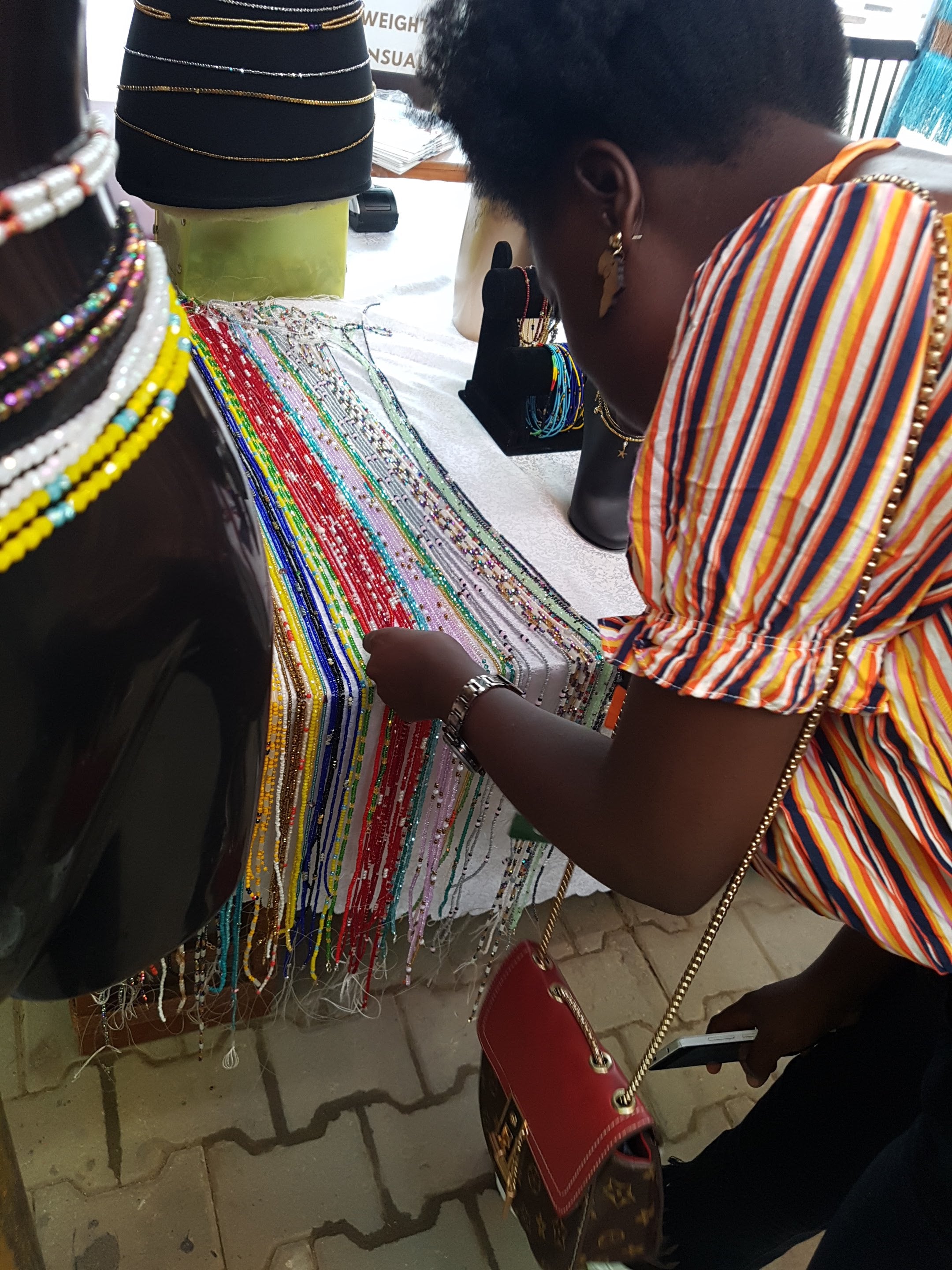 Black Woman Choosing Waist Beads Of Different Colours Lined Up On A Table