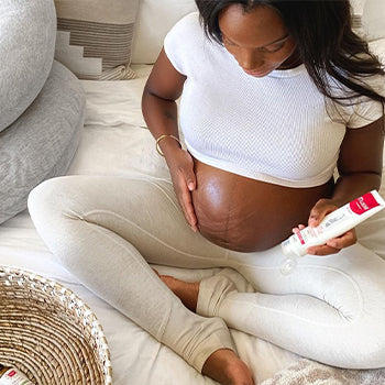 Woman applying cream on belly at 5 months pregnant