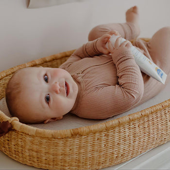 6 month old baby laying down on back holding Mustela products