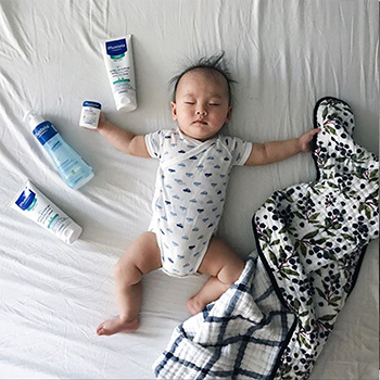 baby on bed with Mustela skincare products