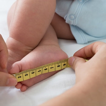 Parent measuring baby foot and comparing it to a baby growth chart